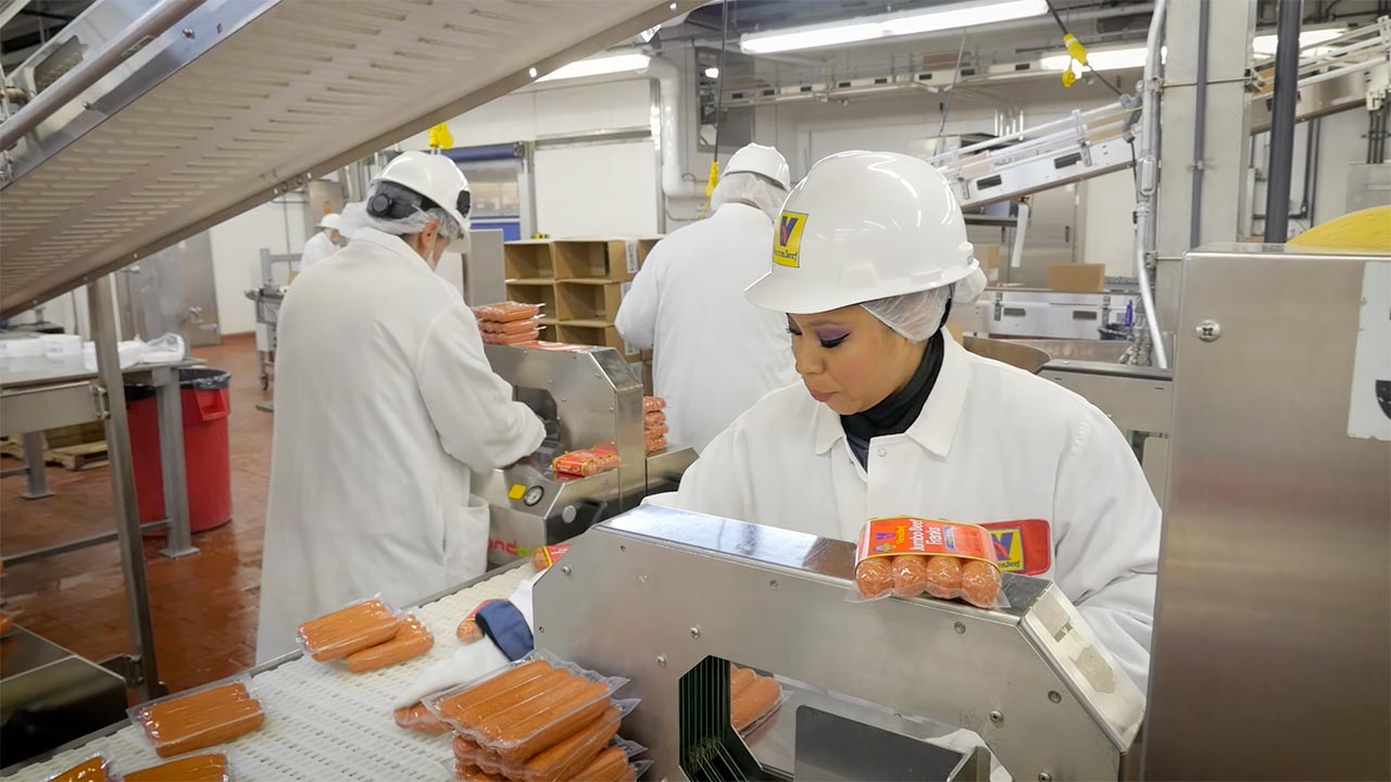 Workers at Vienna Beef factory examine hot dog franks on conveyor belt