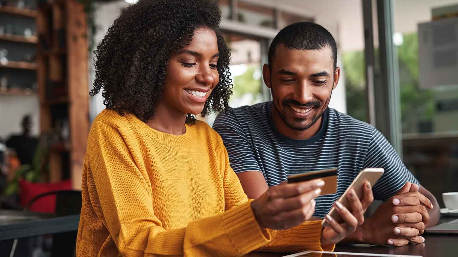 two smiling people using their card on their cellphone