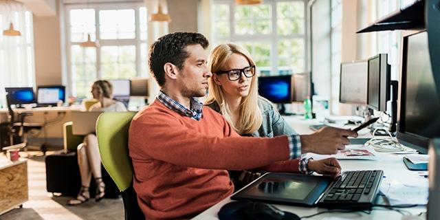 two coworkers looking at a desktop and working together