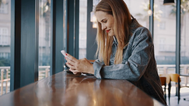 woman scrolls cell phone while seated at counter