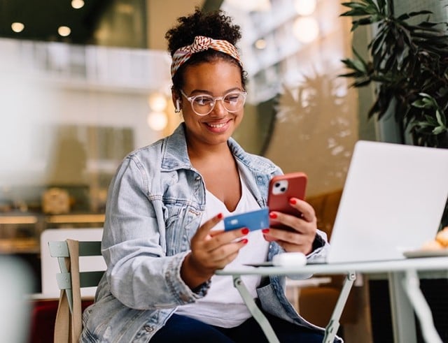 woman holding her smartphone and card while she's doing a transaction