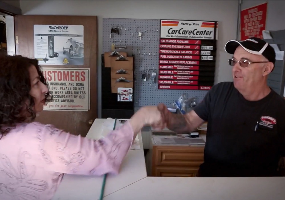 woman in pink shirt shakes hands with mechanic