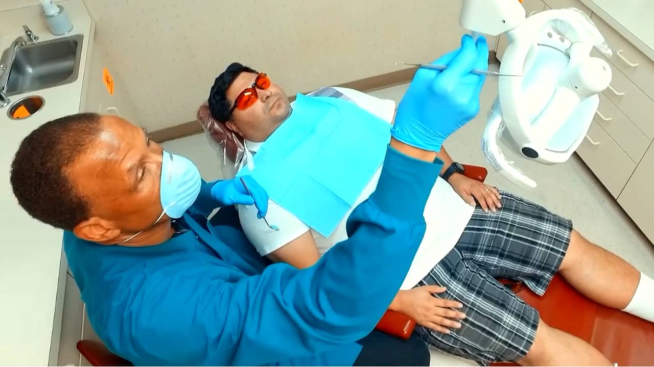 Dental hygienist in scrubs prepares to clean teeth for male patient in chair