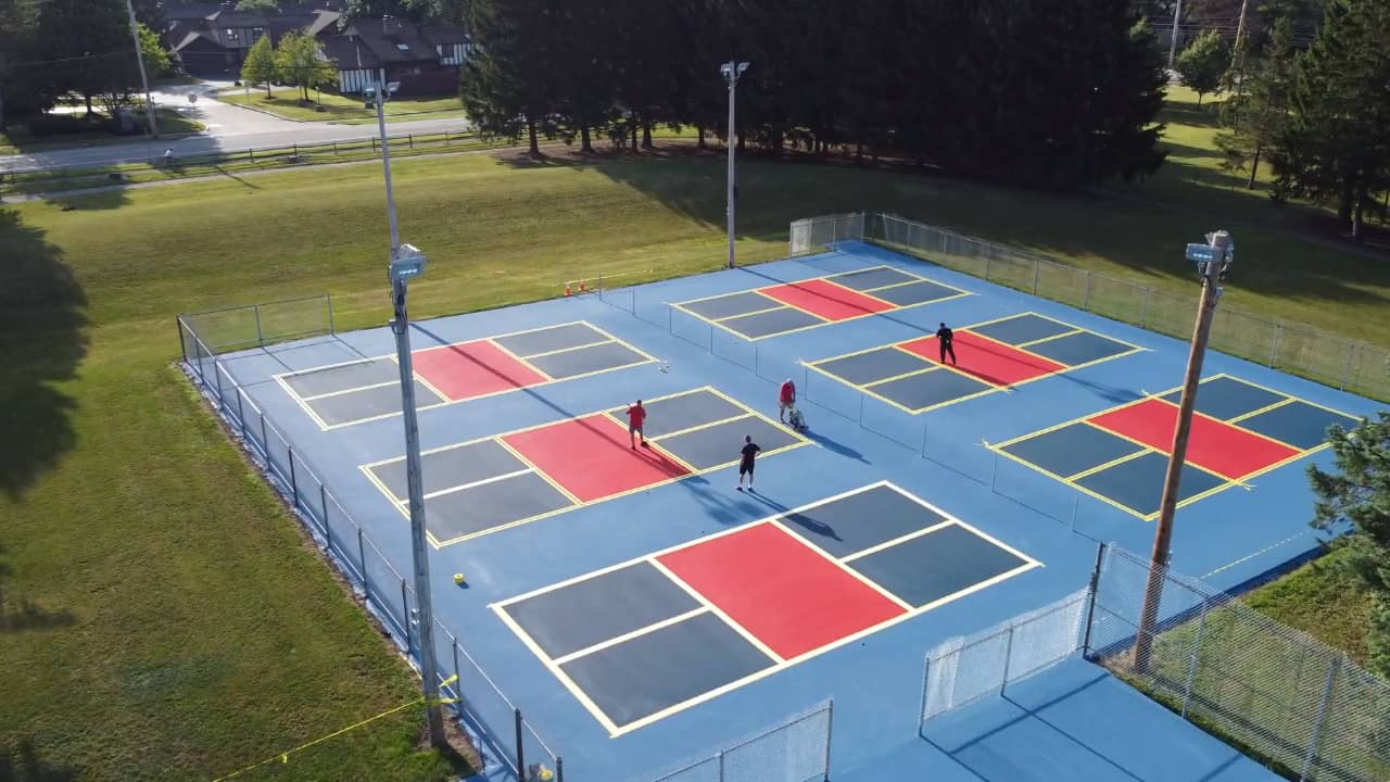Construction workers paint and seal coat pickleball courts