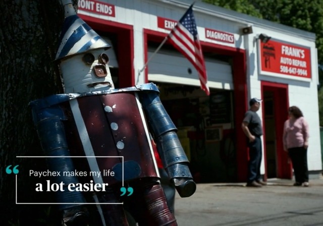 Tin Man made of oil cans with mechanic and female in background of car repair shop
