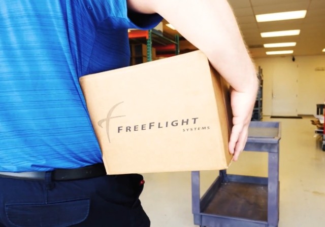 man carries box labeled "Freeflight" under arm